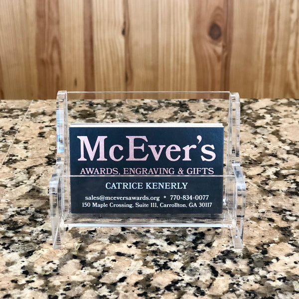 Clear acrylic bench shaped business card holder for table top. Holding a stack of black business cards.