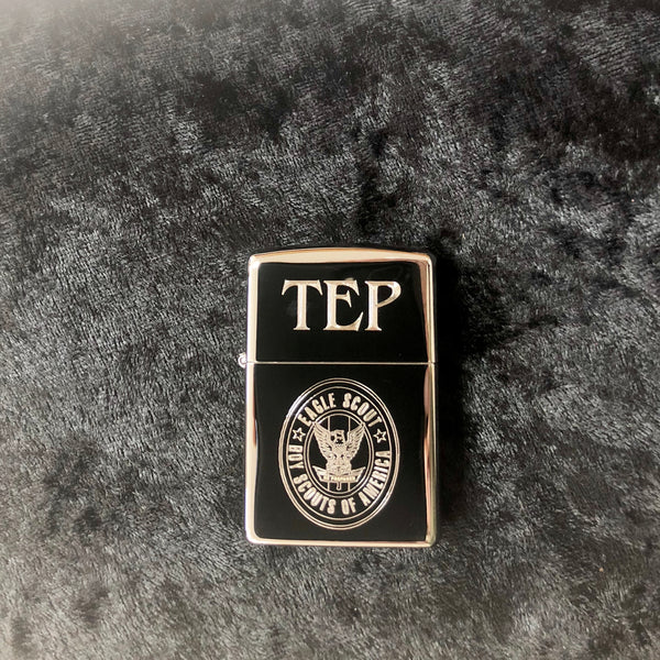 Shiny silver stainless steel lighter engraved with an eagle scout log on the bottom, and a monogram on the top.
