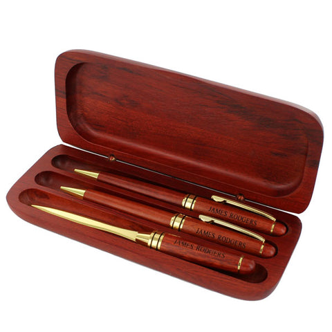 Hinged rosewood box that has three slots each holding a rosewood pen, pencil, or letter opener. Pen and pencil feature shiny gold tips, middle rings and clips. Letter opener has a shiny gold sharp edge. Each of the handles is engraved with "James Rodgers" in black letters. Case can be engraved as well.