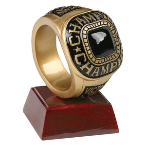 Champion trophy featuring a square shaped maroon glossy base with a large gold and black ring sitting on top vertically. The ring has a black faux stone and says "CHAMPION" around the center.