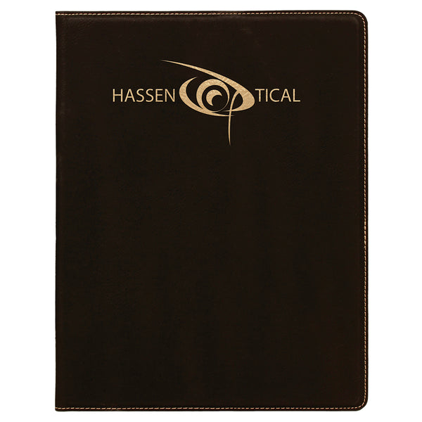 Small black leatherette portfolio. The front of the portfolio is engraved with a gold company logo at the top center. The portfolio opens up to reveal a lined white note pad.