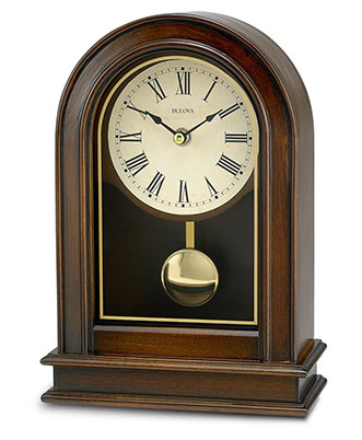 Walnut colored wooden rectangluar bottom clock with curved top featuring a shiny gold pendulum, glass cover, and a cream colored face with black roman numerals.