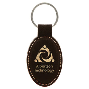 Oval shaped black leatherette keychain with gold engraving. There is gold stitching around the edge to match the gold company logo engraved. Silver key ring attached.