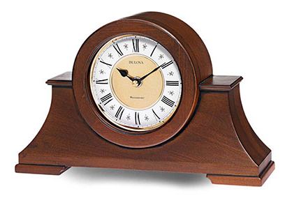 Large walnut colored wooden mantel clock with a white and gold face featuring black roman numerals.