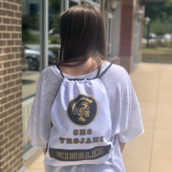 A white drawstring bag engaved with a school logo, school name, and last name on the back of a girl with a white shirt on.