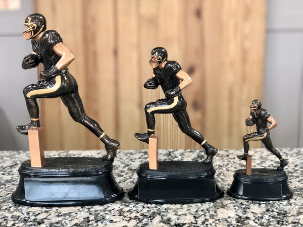 Large, medium, and small black and bronze football trophies with oval bases and running football players. From left to right displaying the different sizes.