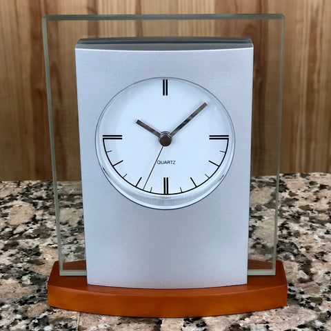 Silver and glass clock with light wood base featuring a white face with silver hands.