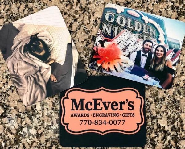 Three mouse pads engraved with photos. One mouse pad features a photo of a dog, another is engraved with a black and bronze company logo, and one is engraved with a photo of a man and woman at a wedding.
