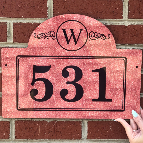 Rust colored rectangle mail box sign engrav ed with large black numbers in the center. The top of the sign is a semi circle shape and features a "W" with a circle and scroll design.