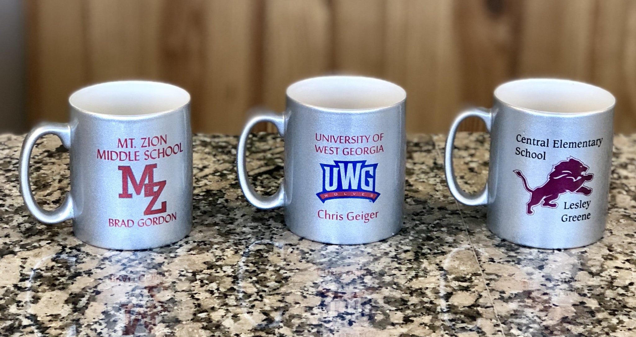 Three silver sparkle glass coffee mugs each engraved with a different school logo and name.
