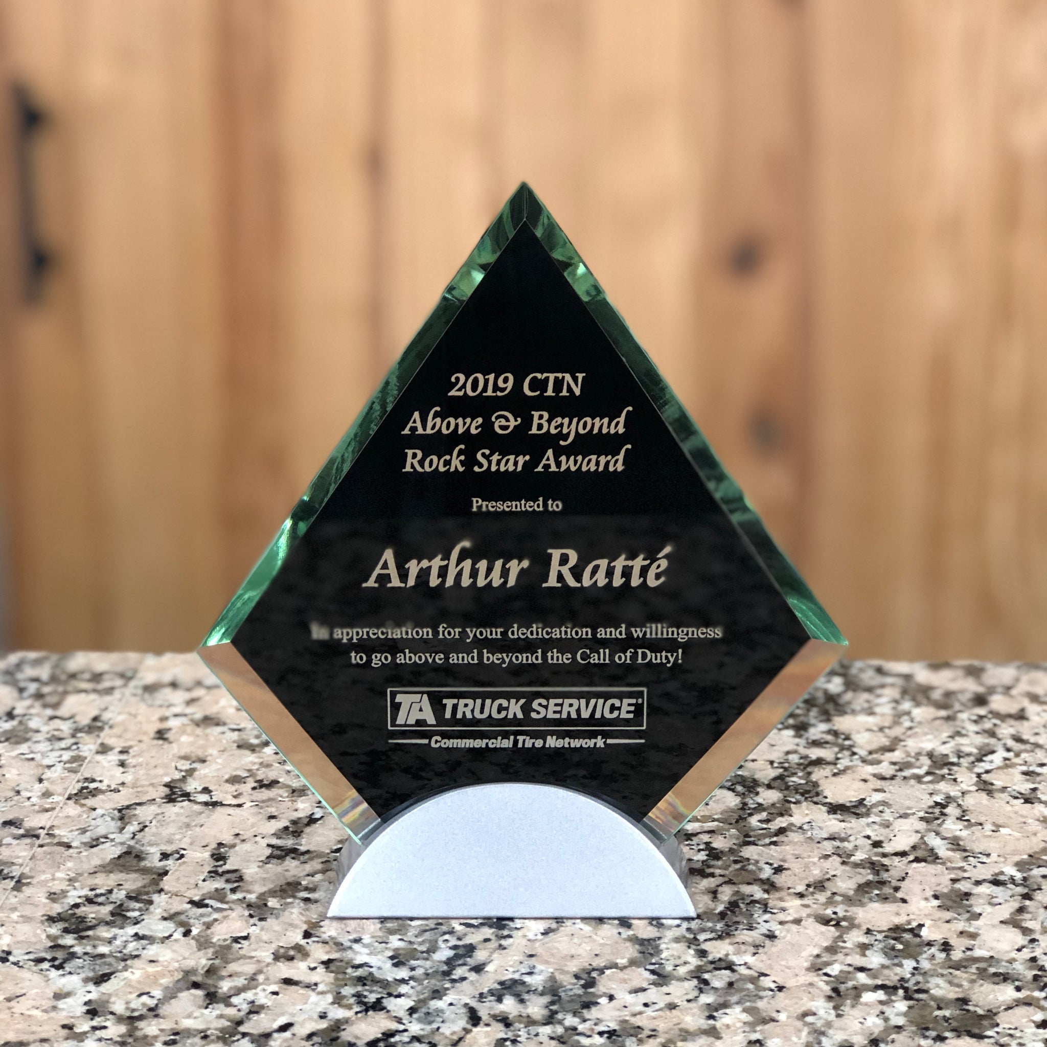 Small diamond shaped black glass award with clear glass edges and engraving. The award is black in the center and sits on a silver stand.