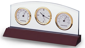 Cherry wood colored long base that has a skinny clear glass piece attached and houses a clock, thermometer, and hygrometer all outlined in shiny gold with white faces and black hands and numbers.